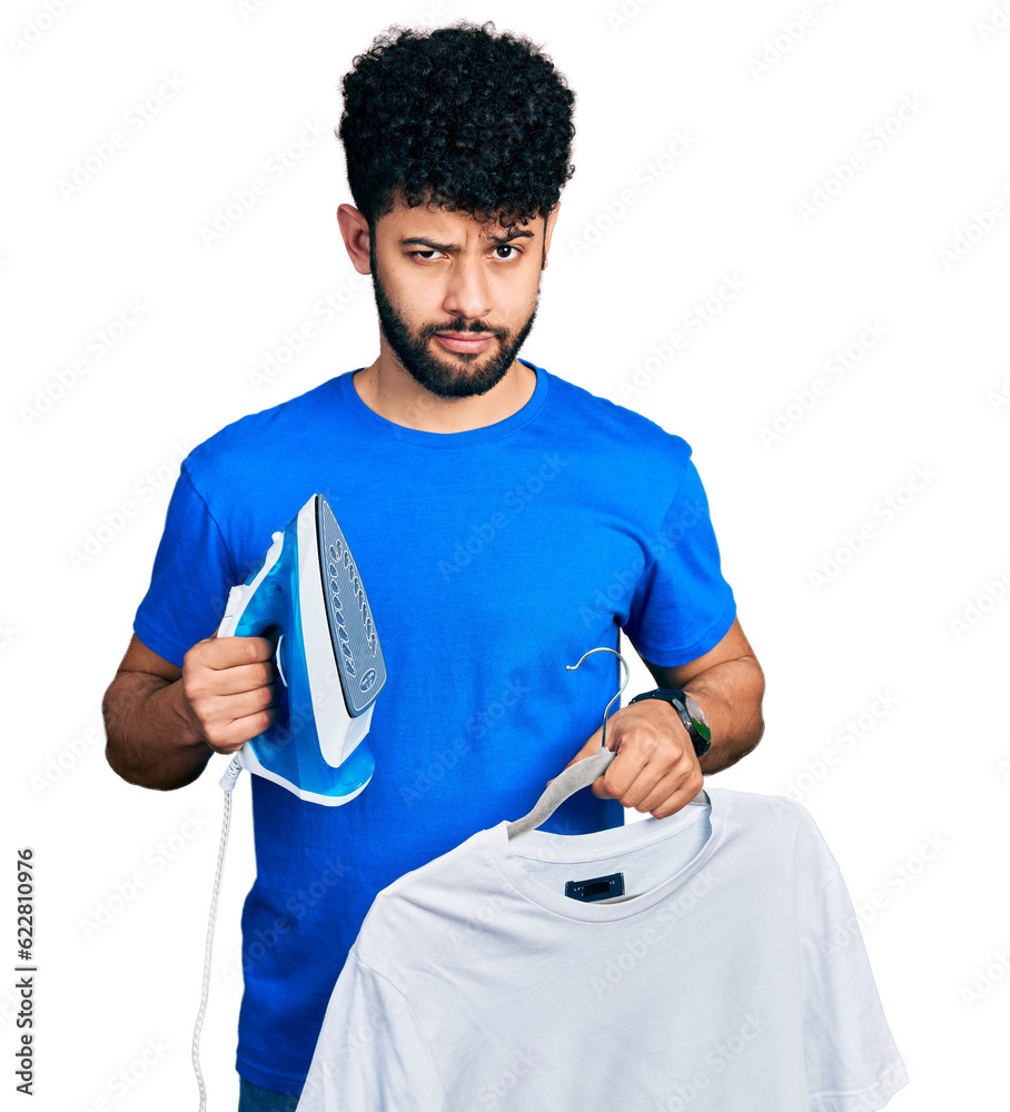 Sticker young arab man with beard holding electric steam iron and white t shirt skeptic and nervous, frownin