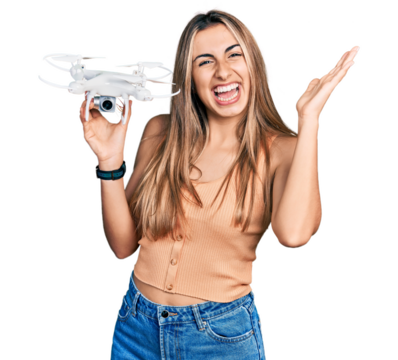 Hispanic young woman holding drone celebrating victory with happy smile and winner expression with raised hands