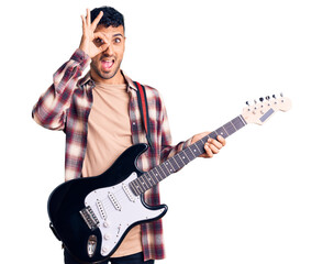 Young hispanic man playing electric guitar smiling happy doing ok sign with hand on eye looking through fingers