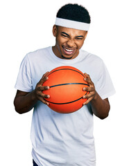 Young african american man holding basketball ball smiling and laughing hard out loud because funny crazy joke.