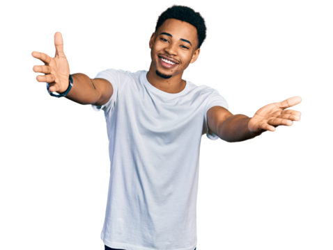 Young african american man wearing casual white t shirt looking at the camera smiling with open arms for hug. cheerful expression embracing happiness.