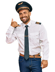 Handsome man with beard wearing airplane pilot uniform smiling doing phone gesture with hand and fingers like talking on the telephone. communicating concepts.