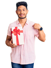 Handsome latin american young man holding gift pointing finger to one self smiling happy and proud