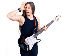 Fototapeta premium Young adult man with long hair playing electric guitar smiling happy doing ok sign with hand on eye looking through fingers