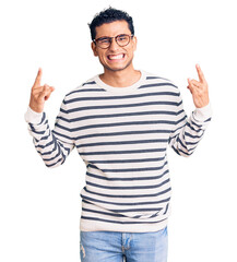 Hispanic handsome young man wearing casual clothes and glasses shouting with crazy expression doing rock symbol with hands up. music star. heavy concept.