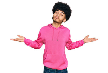 Young african american man with afro hair wearing casual pink sweatshirt clueless and confused...