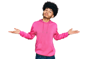Young african american man with afro hair wearing casual pink sweatshirt clueless and confused expression with arms and hands raised. doubt concept.