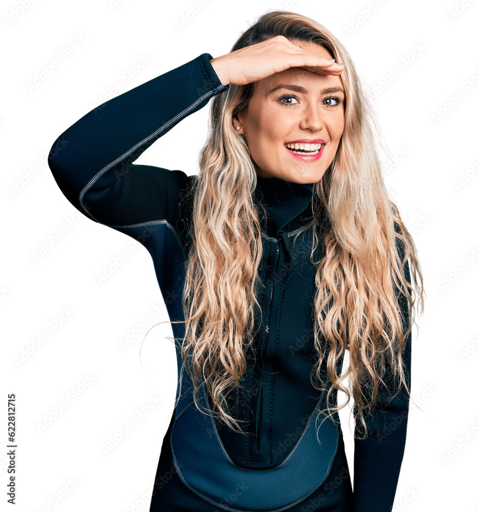 Sticker Young blonde woman wearing diver neoprene uniform very happy and smiling looking far away with hand over head. searching concept.