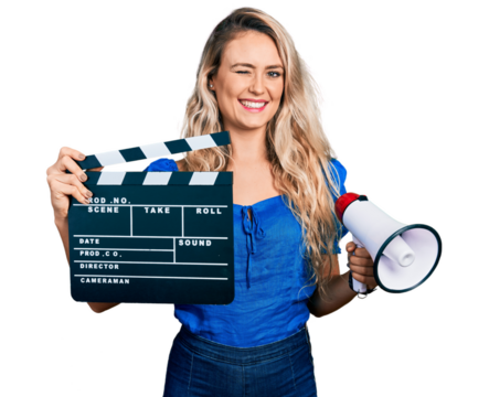 Young blonde woman holding video film clapboard and megaphone winking looking at the camera with sexy expression, cheerful and happy face.