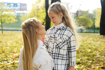 Fototapeta premium Mother and daughter spend time together in the autumn park. Mother lovingly looks at her daughter