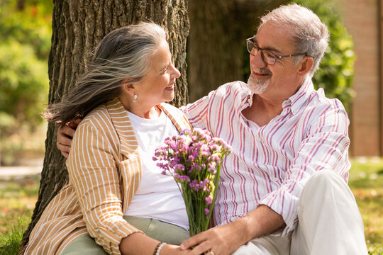 Happy senior european man gives bouquet of flowers to woman, enjoy romantic date together in park, outdoor