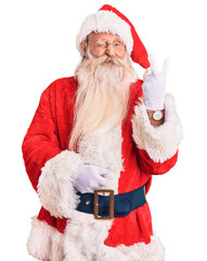 Old senior man with grey hair and long beard wearing traditional santa claus costume smiling with...