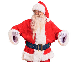 Old senior man with grey hair and long beard wearing traditional santa claus costume pointing down looking sad and upset, indicating direction with fingers, unhappy and depressed.