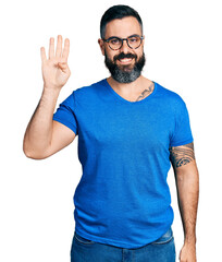 Fototapeta premium Hispanic man with beard wearing casual t shirt and glasses showing and pointing up with fingers number four while smiling confident and happy.
