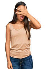 Beautiful hispanic woman wearing casual clothes peeking in shock covering face and eyes with hand, looking through fingers with embarrassed expression.