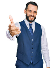 Young man with beard wearing business vest smiling friendly offering handshake as greeting and welcoming. successful business.