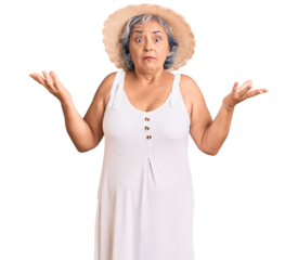 Senior woman with gray hair wearing summer hat and summer clothes clueless and confused expression with arms and hands raised. doubt concept.