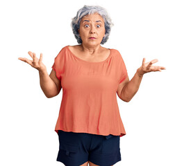 Senior woman with gray hair wearing orange tshirt clueless and confused expression with arms and hands raised. doubt concept.