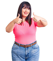 Young plus size woman wearing casual clothes approving doing positive gesture with hand, thumbs up smiling and happy for success. winner gesture.