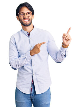 Handsome hispanic man wearing business shirt and glasses pointing aside worried and nervous with both hands, concerned and surprised expression