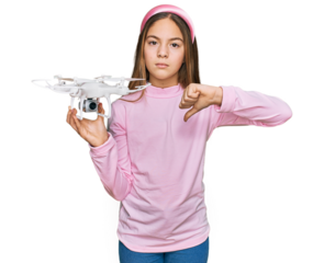 Beautiful brunette little girl using drone with angry face, negative sign showing dislike with thumbs down, rejection concept