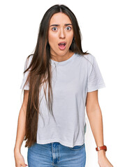 Fototapeta premium Young hispanic girl wearing casual white t shirt afraid and shocked with surprise and amazed expression, fear and excited face.