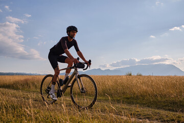 Fototapeta na wymiar Male cyclist wearing cycling kit and helmet riding on the road a gravel bike at sunset.Sports motivation image.