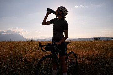 Female cyclist in cycling clothes and a helmet drinks water from a sports bottle.