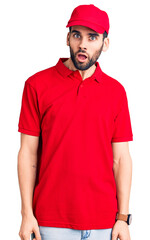 Young handsome man with beard wearing delivery uniform in shock face, looking skeptical and sarcastic, surprised with open mouth