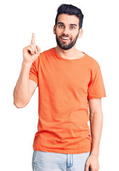 Young handsome man with beard wearing casual t-shirt pointing finger up with successful idea. exited and happy. number one.