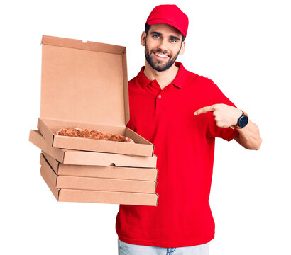 Young handsome man with beard wearing delivery uniform holding boxes with pizza pointing finger to one self smiling happy and proud