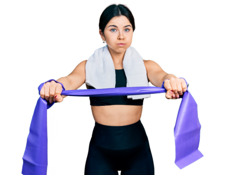Young brunette woman with blue eyes training arm resistance with elastic arm bands puffing cheeks with funny face. mouth inflated with air, catching air.