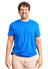 Obraz premium Young handsome man with curly hair wearing casual clothes sticking tongue out happy with funny expression. emotion concept.
