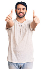 Young hispanic man wearing casual clothes approving doing positive gesture with hand, thumbs up smiling and happy for success. winner gesture.