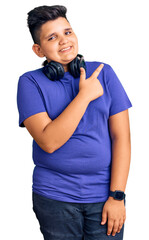 Little boy kid listening to music wearing headphones cheerful with a smile of face pointing with hand and finger up to the side with happy and natural expression on face