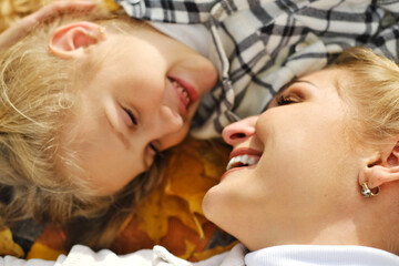 The family has fun in the park. Girl and mother lie on a blanket, look at each other and smile