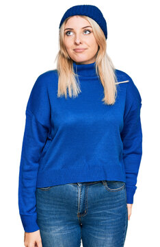 Young caucasian woman wearing wool winter sweater and cap smiling looking to the side and staring away thinking.