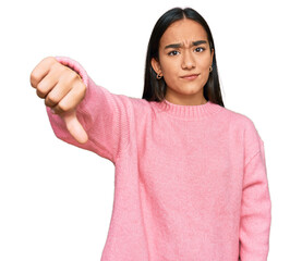 Young asian woman wearing casual winter sweater looking unhappy and angry showing rejection and negative with thumbs down gesture. bad expression.