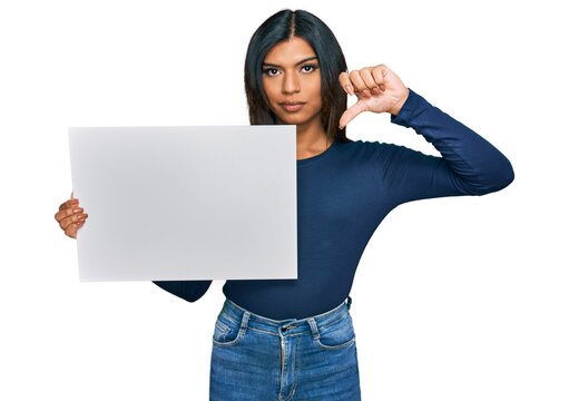 Young latin transsexual transgender woman holding blank empty banner with angry face, negative sign showing dislike with thumbs down, rejection concept