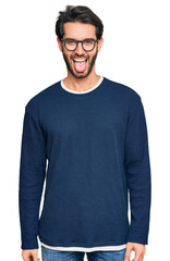 Fototapeta premium Young hispanic man wearing casual clothes and glasses sticking tongue out happy with funny expression. emotion concept.