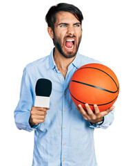 Hispanic man with blue eyes holding reporter microphone and basketball ball angry and mad screaming...
