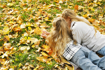 The family has fun in the park. The girl and mother lie on a blanket with their backs to the camera and look at the autumn leaves.