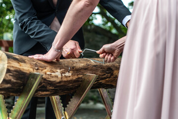 Young bridal couple groom bride sawing a tree trunk together german wedding tradition - 622823566