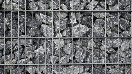 Gabion gefüllt mit grauen Steinen.