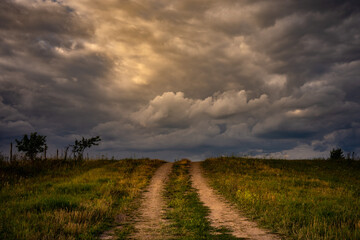 deserted country dirt road up over hilltop under evening dramatic cloudy sky