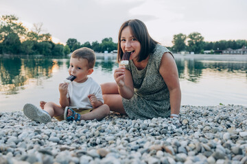 Woman with her son enjoying family time walking  on the lake  together , eating ice cream. Happy family parent with little child boy kid enjoy outdoor lifestyle. Mum and sun eat ice-cream 