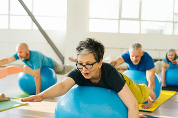 Group of mature friends jumping on blue fitball on yoga class