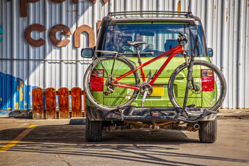 Little green car with red bike on rack parked by metal building - rear view - Colorfu
