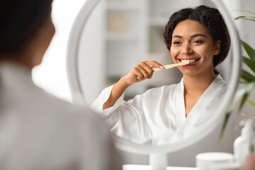Beautiful Young African American Female Brushing Her Teeth With Toothbrush Near Mirror