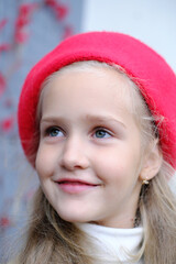 Portrait of a beautiful little girl in a trench coat and a red beret. A girl poses while sitting at a table in a street cafe.